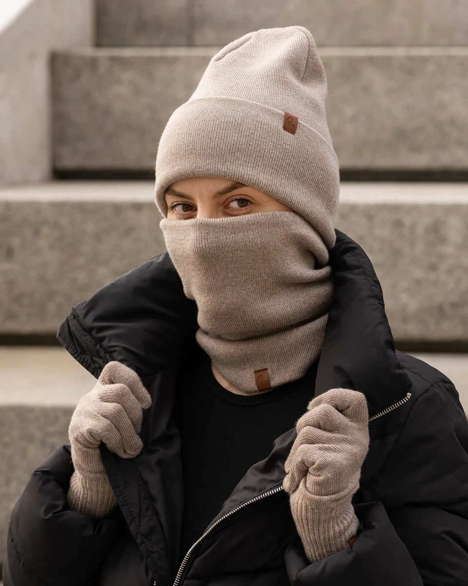Person wearing a beige knit hat, scarf, and gloves sitting on steps.