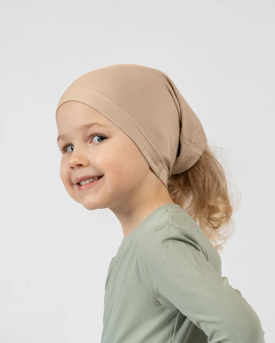 Child wearing a beige headscarf on a white background