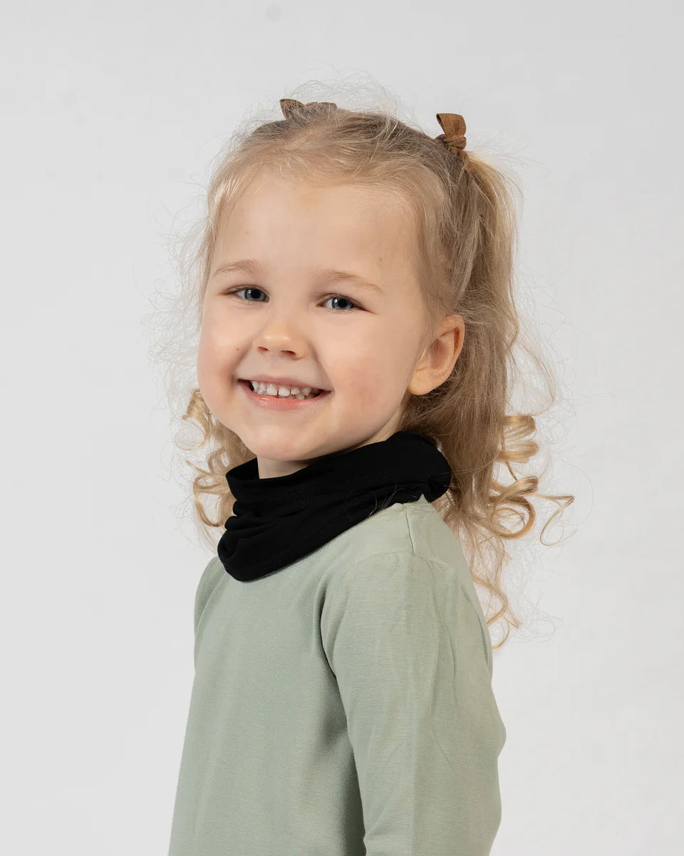 Young girl with pigtails wearing a black turtleneck and green top against a white background