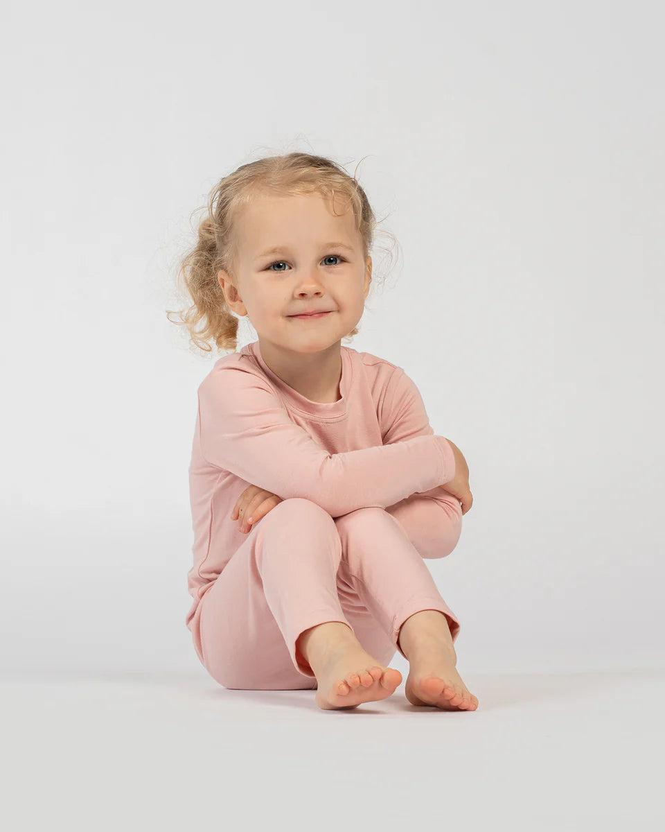 Young child wearing pink pajamas sitting on a white background