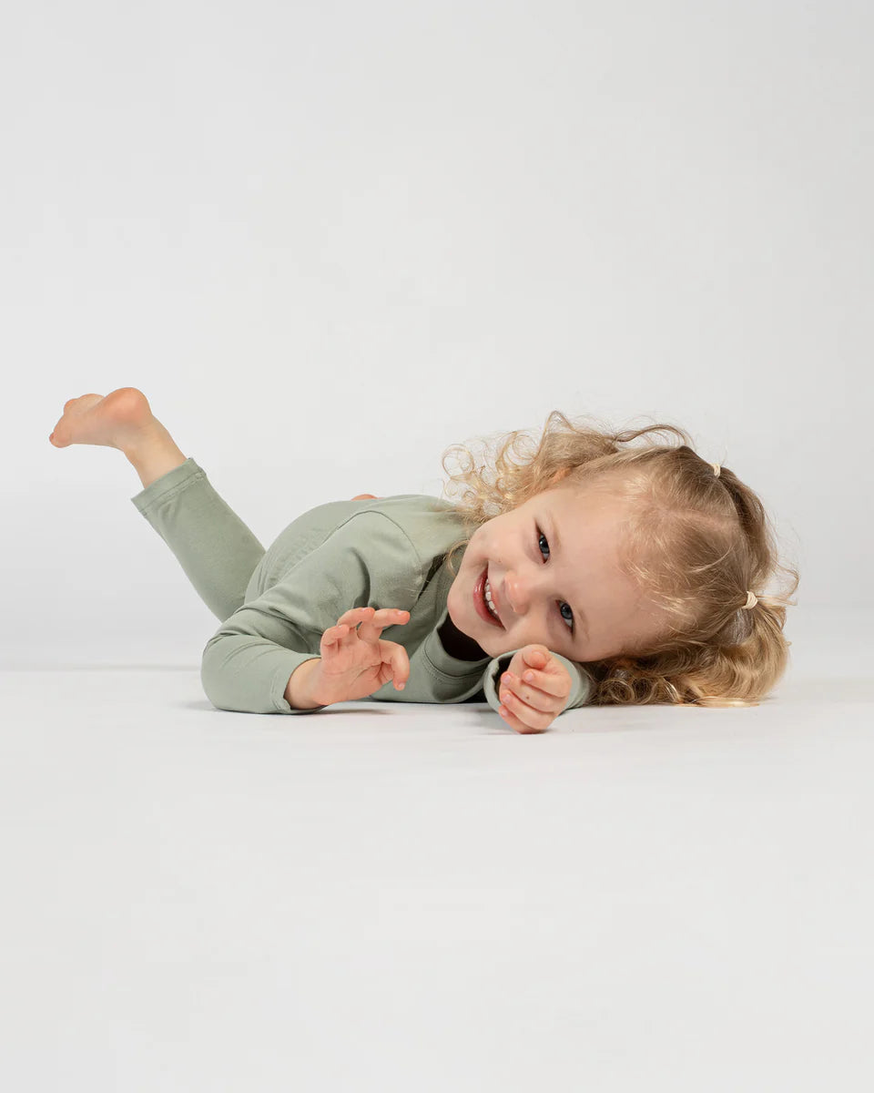 Child in a green outfit lying on a white surface with a plain background