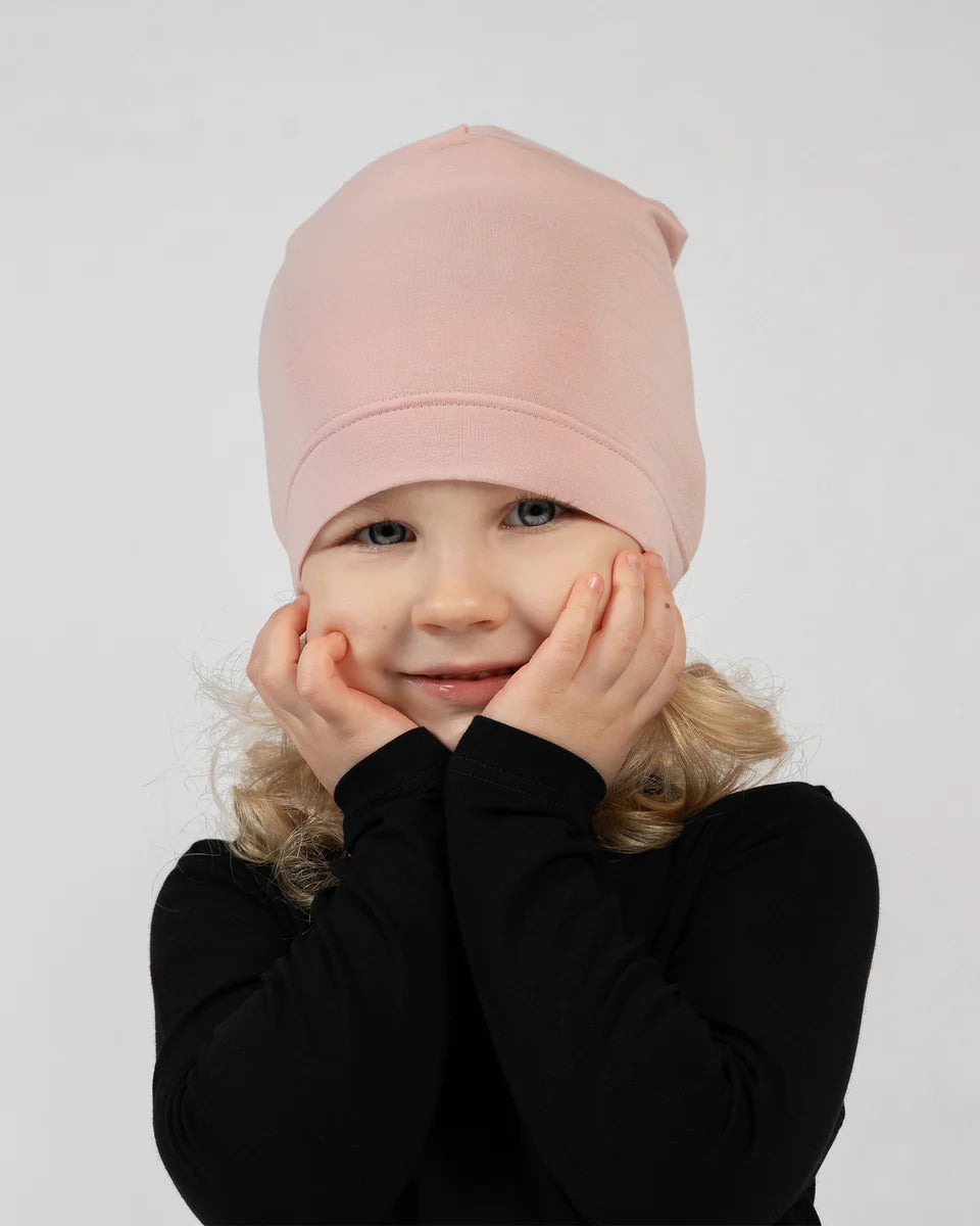 Child wearing a pink beanie and black outfit on a white background