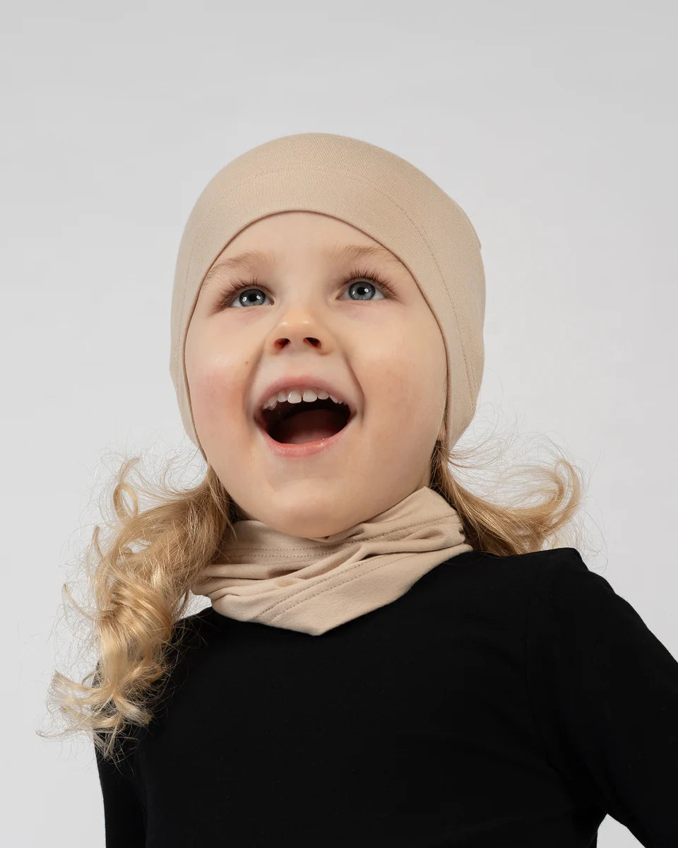 Child wearing a beige headscarf and black outfit on a light gray background