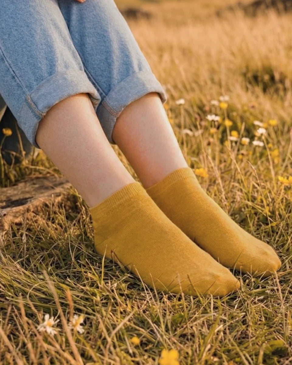 Yellow socks worn with rolled-up jeans on a grassy field.