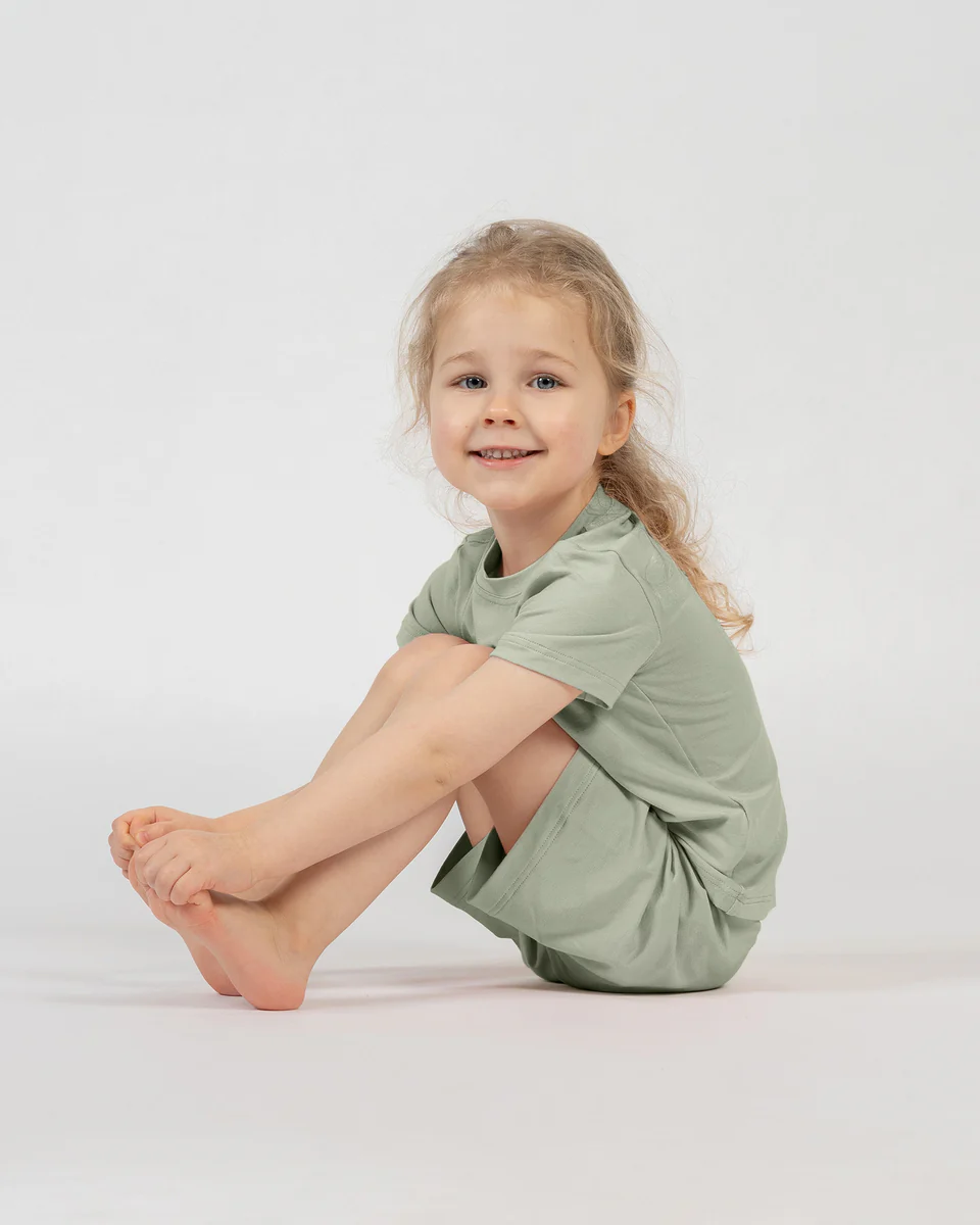 Young girl wearing a green outfit sitting on a white background