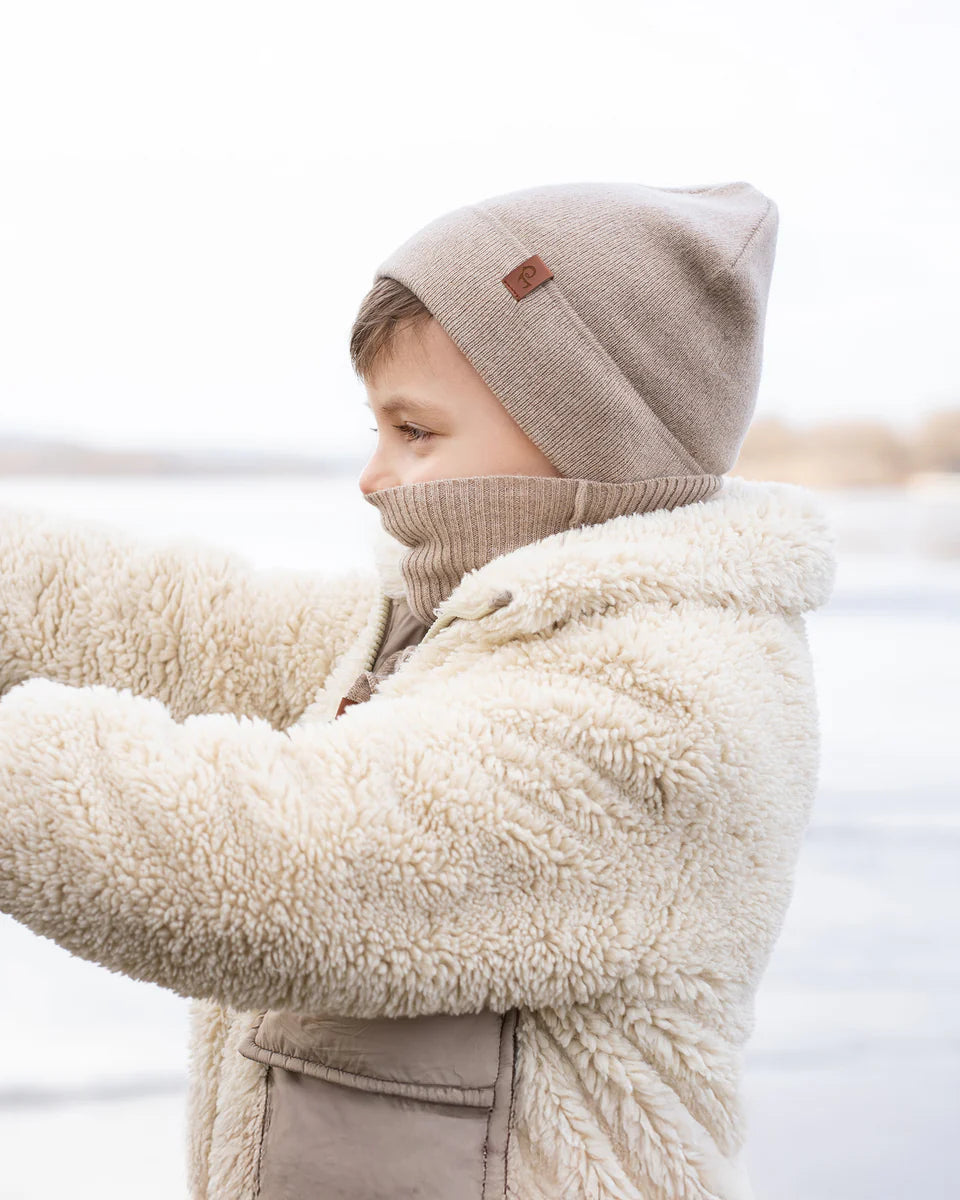 Child wearing a beige knit hat and coat with a blurred natural background