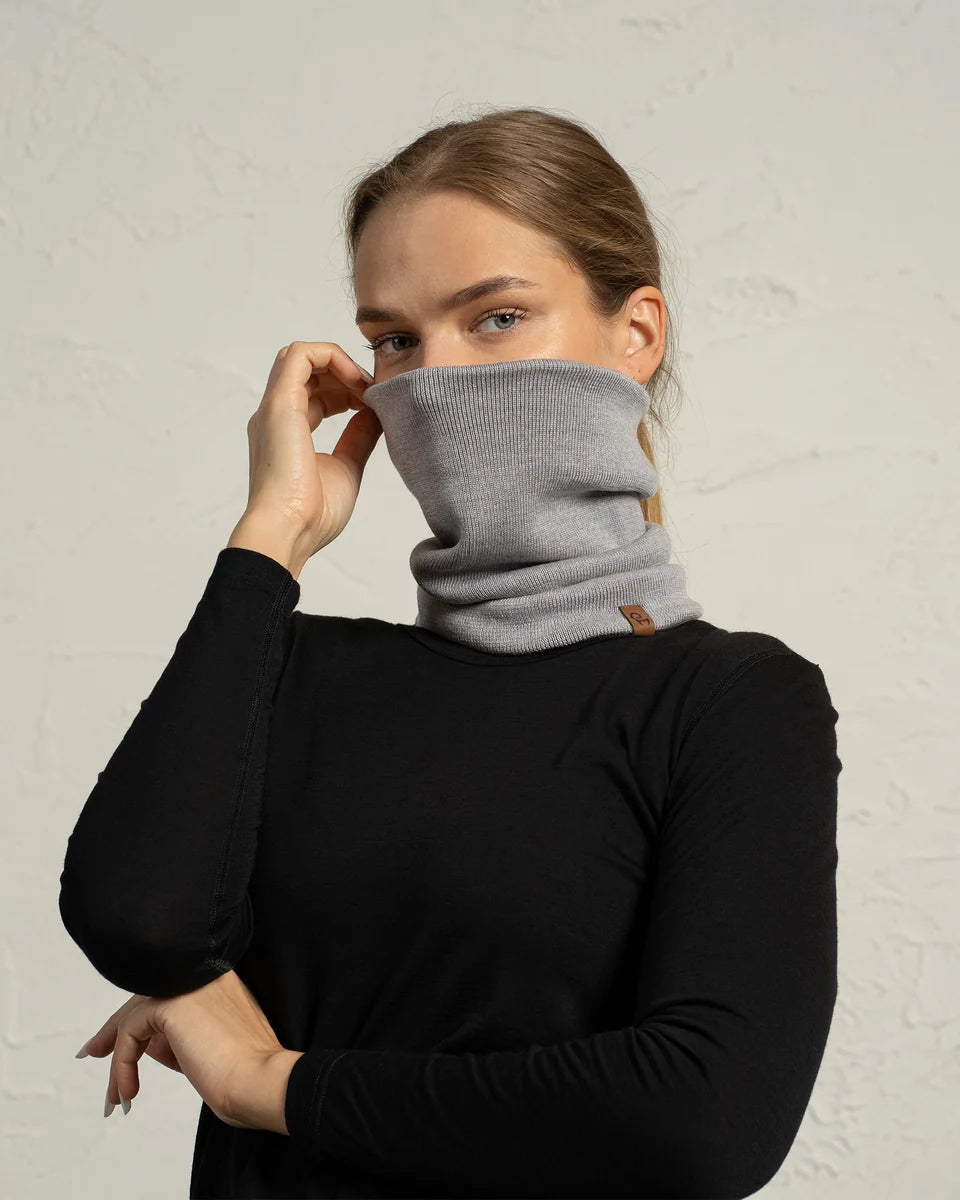 Person wearing a gray cowl neck sweater against a plain background