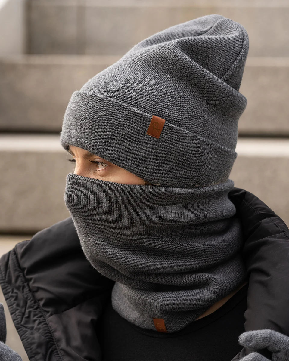 Person wearing a gray beanie and scarf with a brand logo, sitting on steps.