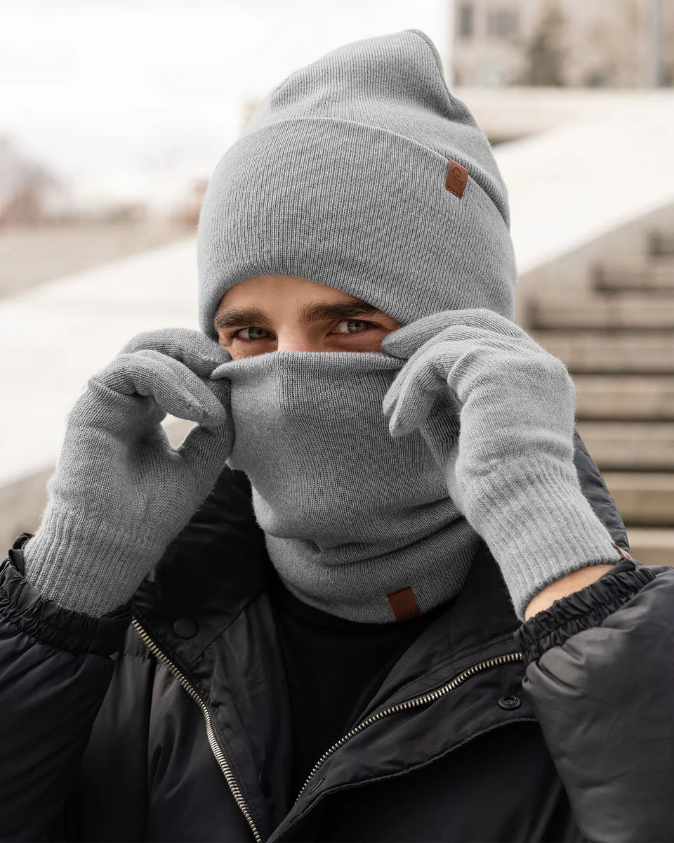Person wearing a gray beanie, scarf, and gloves in an urban setting