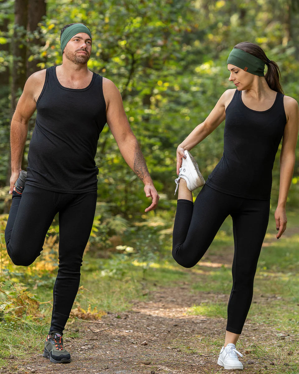 Two people in black athletic wear stretching outdoors on a path with greenery.