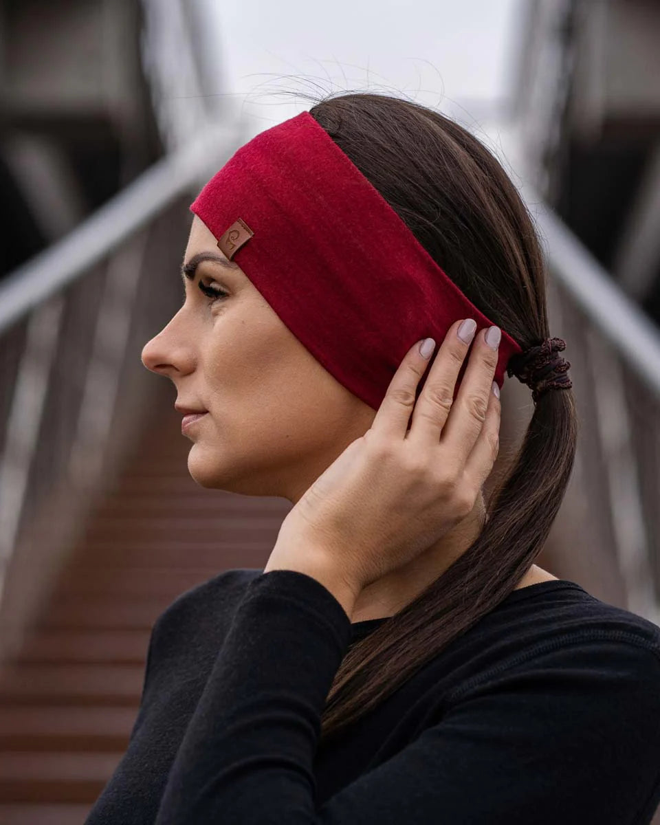 Woman wearing a red headband with a brand logo, adjusting it on her head.