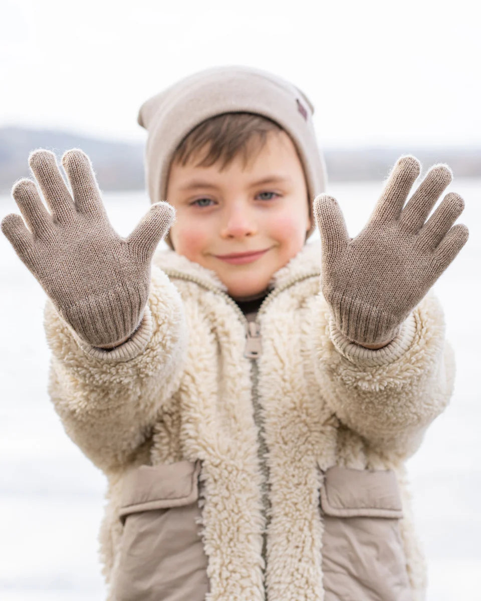 Child wearing a beige coat and gloves with a blurred snowy background