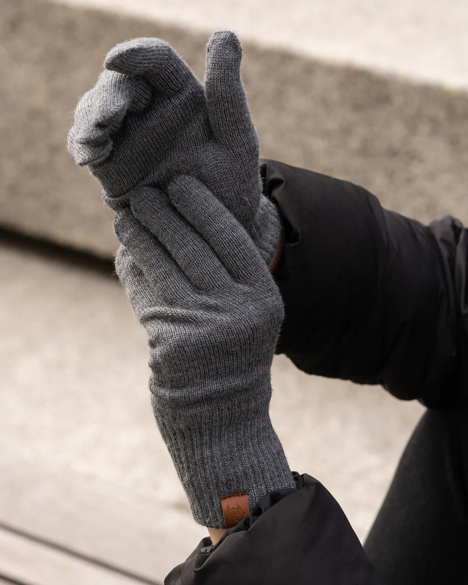 Person wearing gray gloves with a black sleeve, holding one glove up.