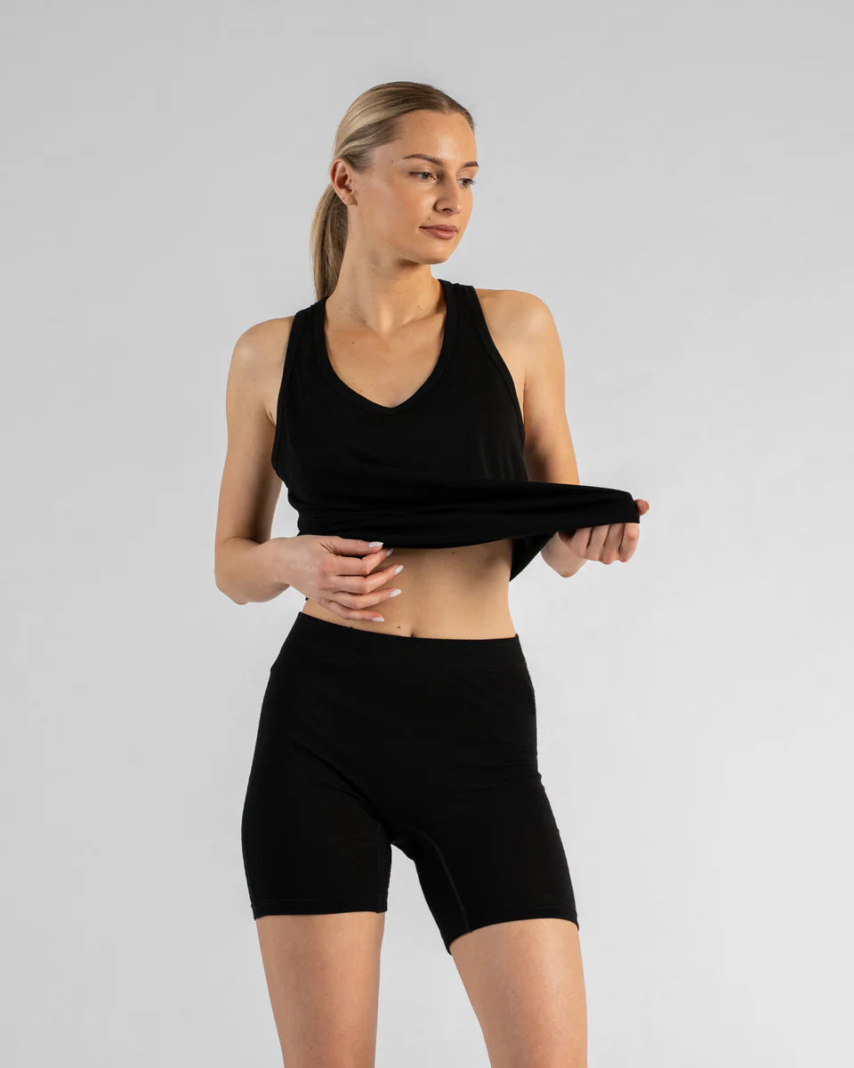 A woman modeling a black athletic crop top and matching black biker shorts against a light gray studio background.