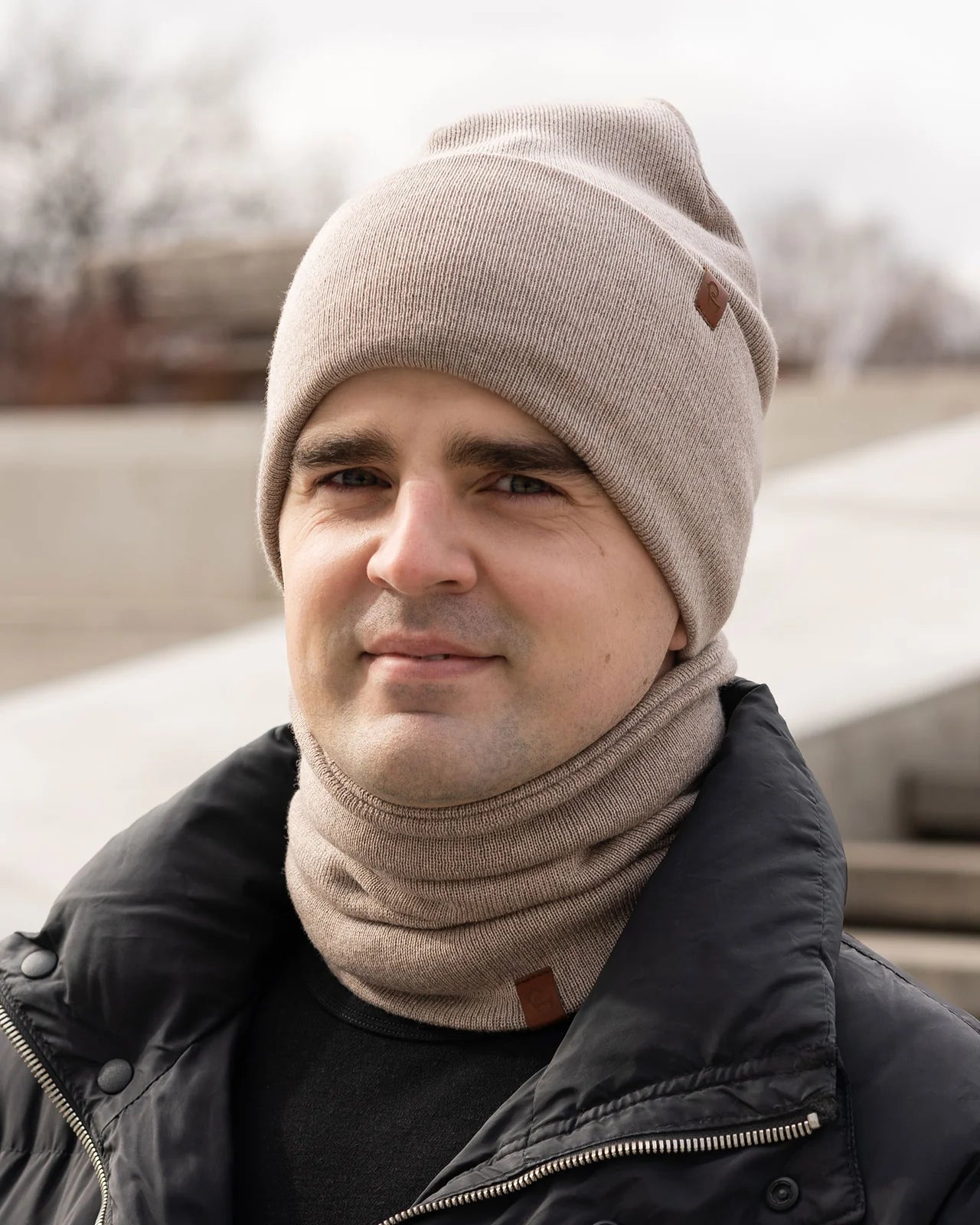 Man wearing a beige knit beanie and scarf in an outdoor setting
