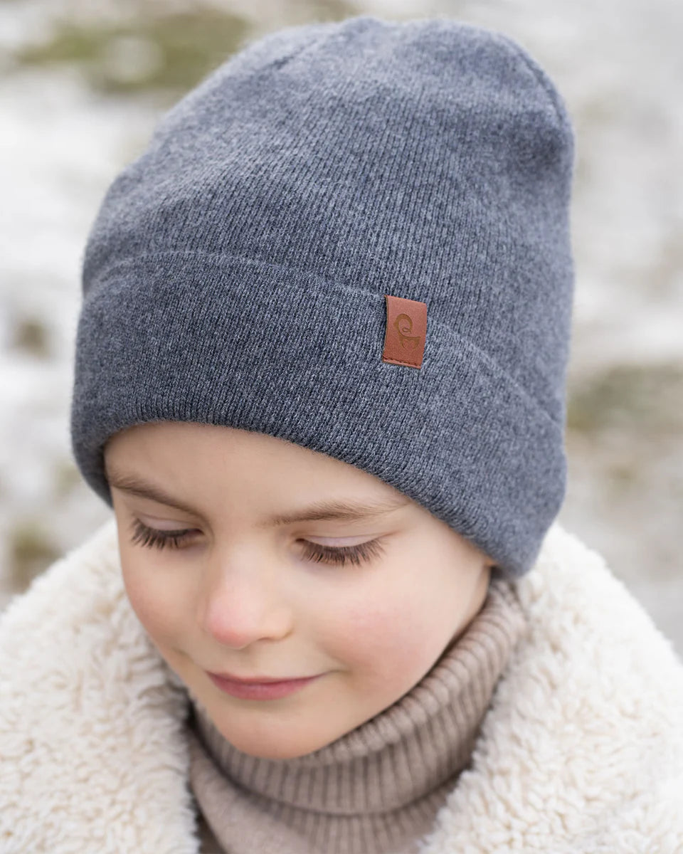 Child wearing a gray knit beanie with a brand logo, standing outdoors.
