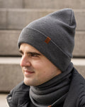 Man wearing a gray knit beanie and scarf against a neutral background