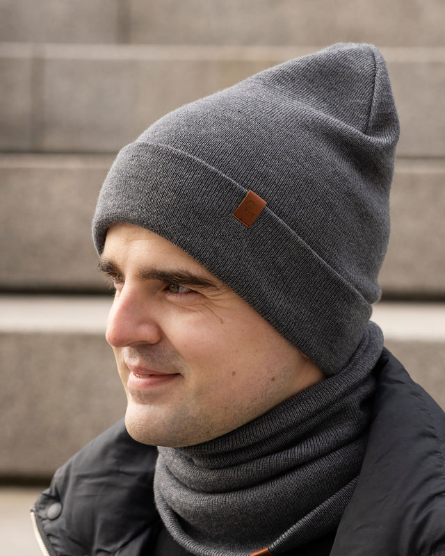 Man wearing a gray knit beanie and scarf against a neutral background