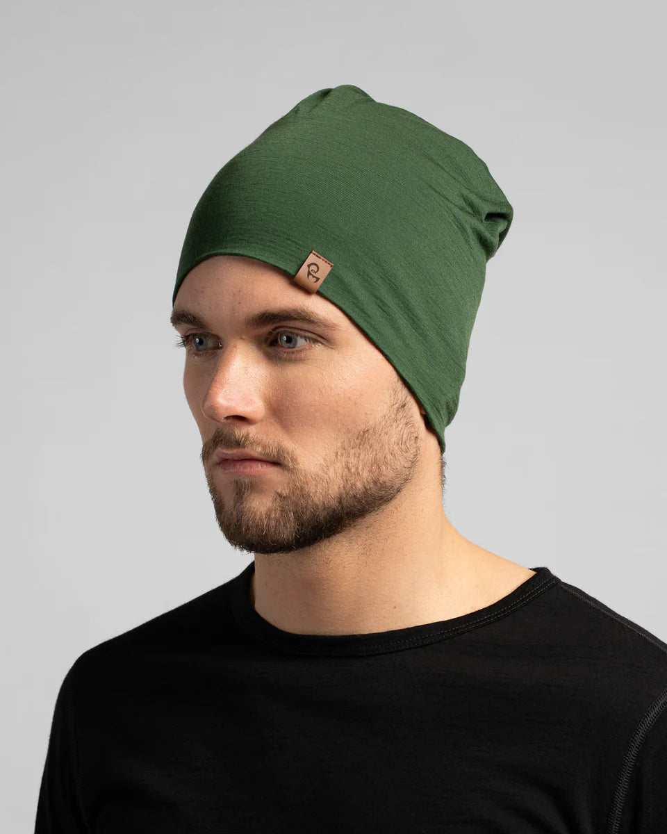 Man wearing a green beanie with a brand logo on a gray background