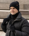 Man wearing a black winter coat, beanie, and gloves standing on steps.