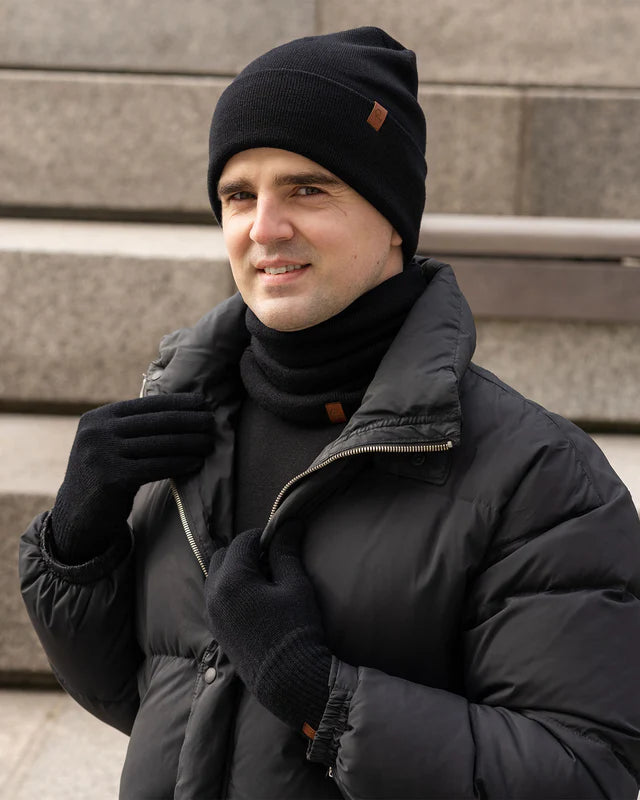 Man wearing a black winter coat, beanie, and gloves standing on steps.
