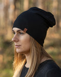 Woman wearing a black beanie with a brand logo in a forest setting