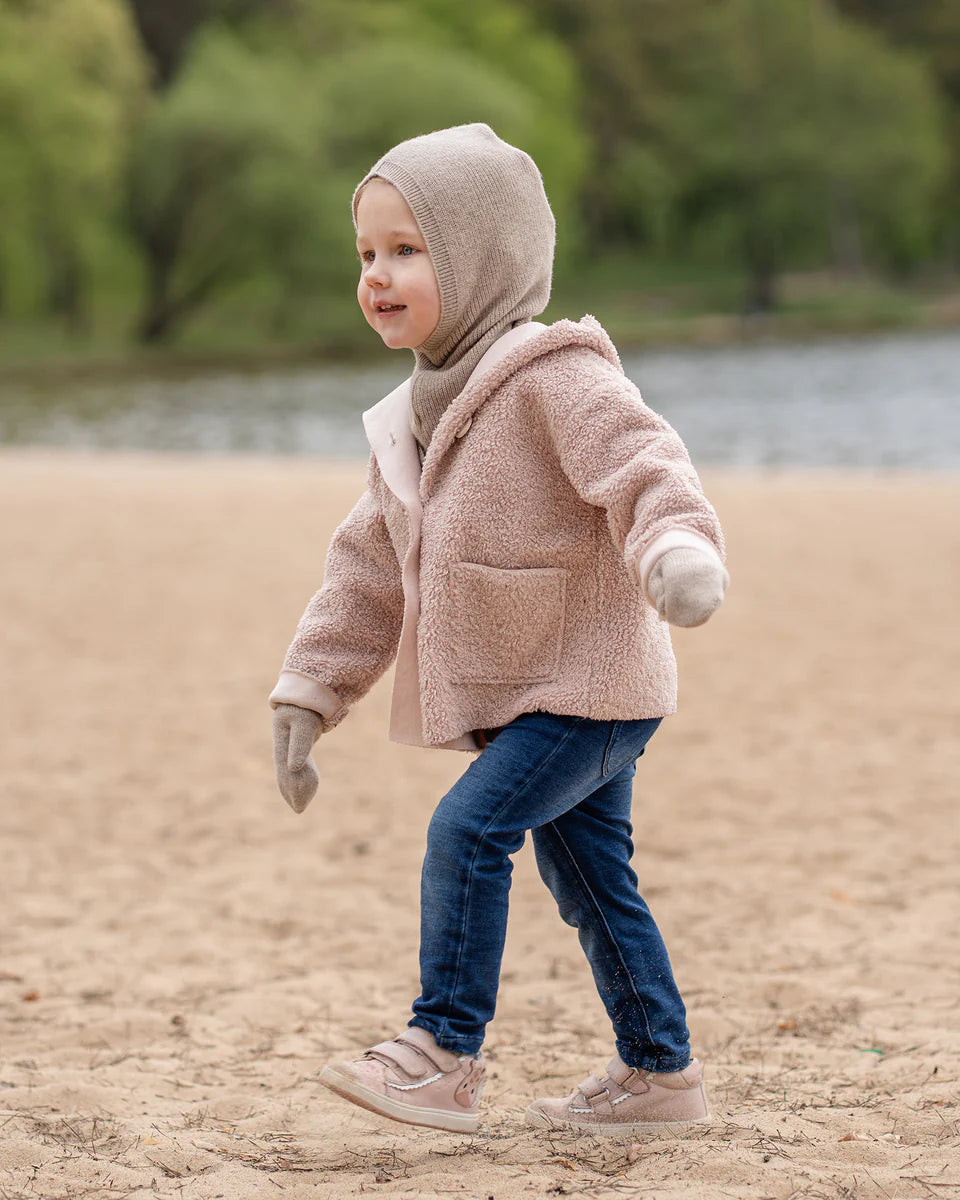 Child wearing a creamy beige knitted merino hooded balaclava on a beach