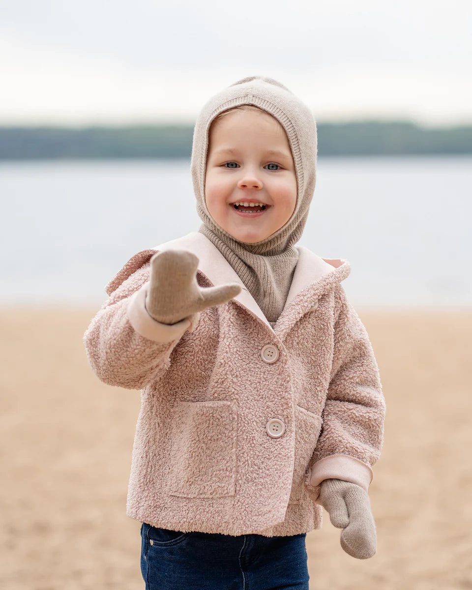 Child wearing a creamy beige knitted merino hooded balaclava by the water