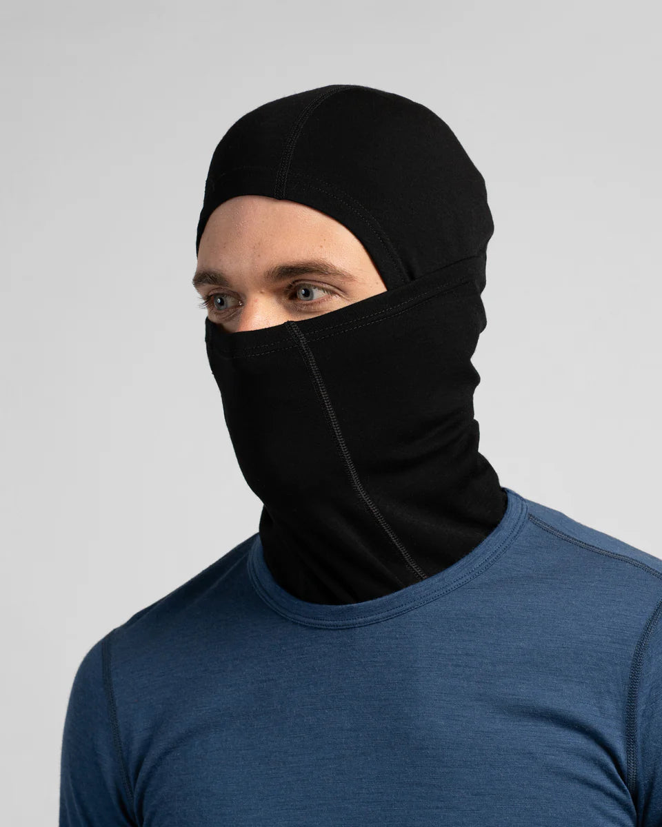 Person wearing a black balaclava over a blue shirt on a light gray background