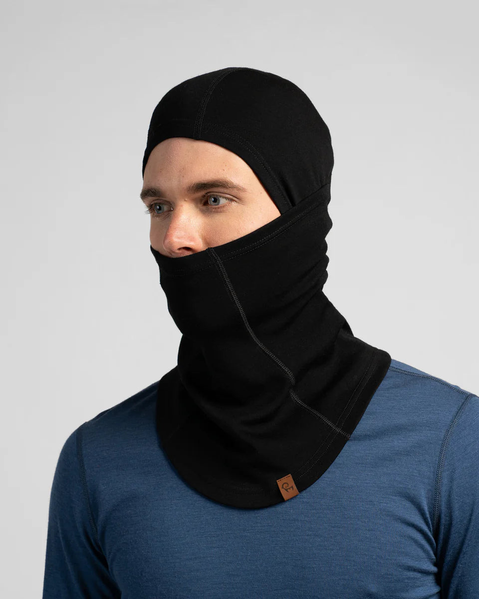 Person wearing a black balaclava over a blue shirt on a gray background