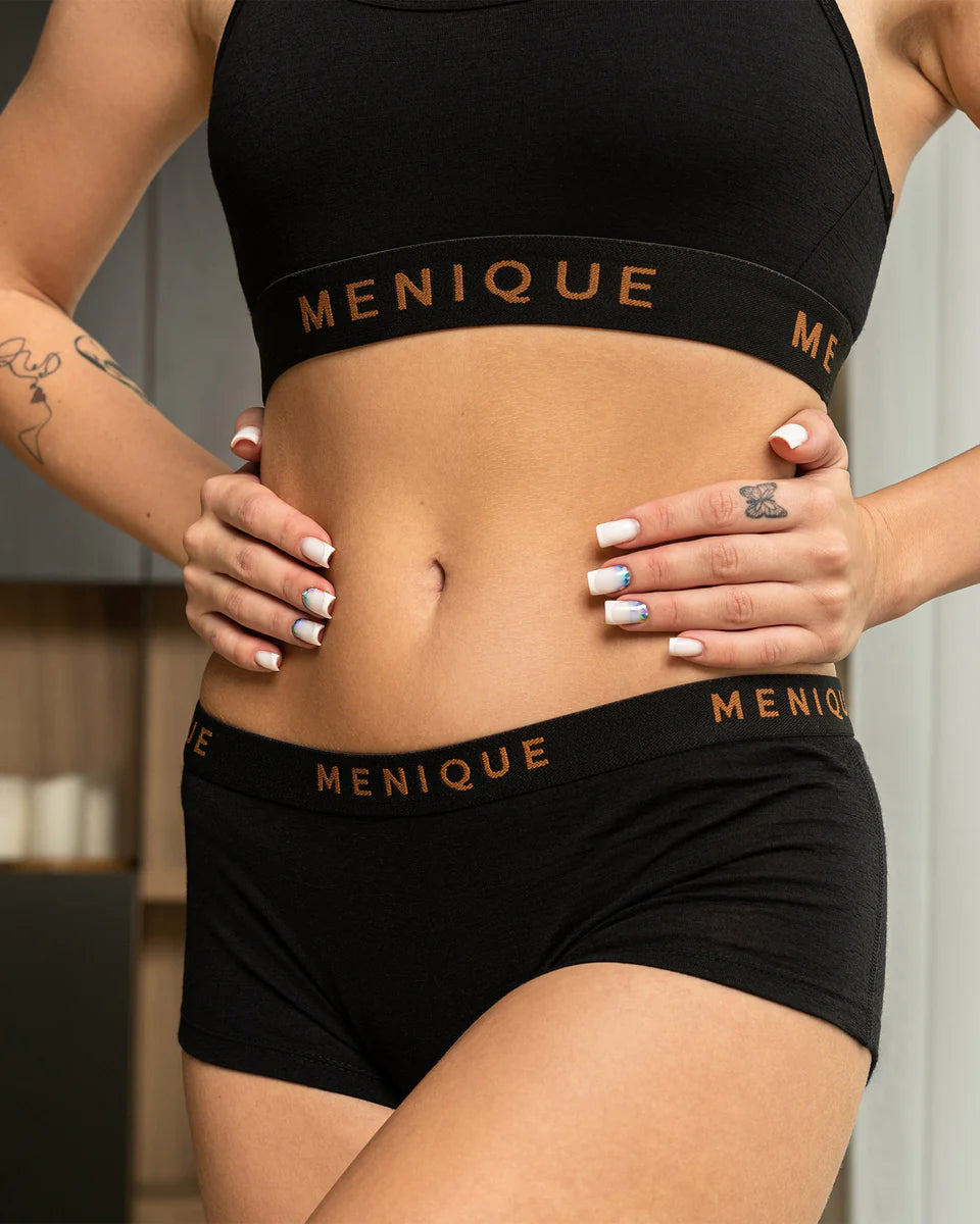 Person wearing black Menique sports bra and shorts with visible branding.