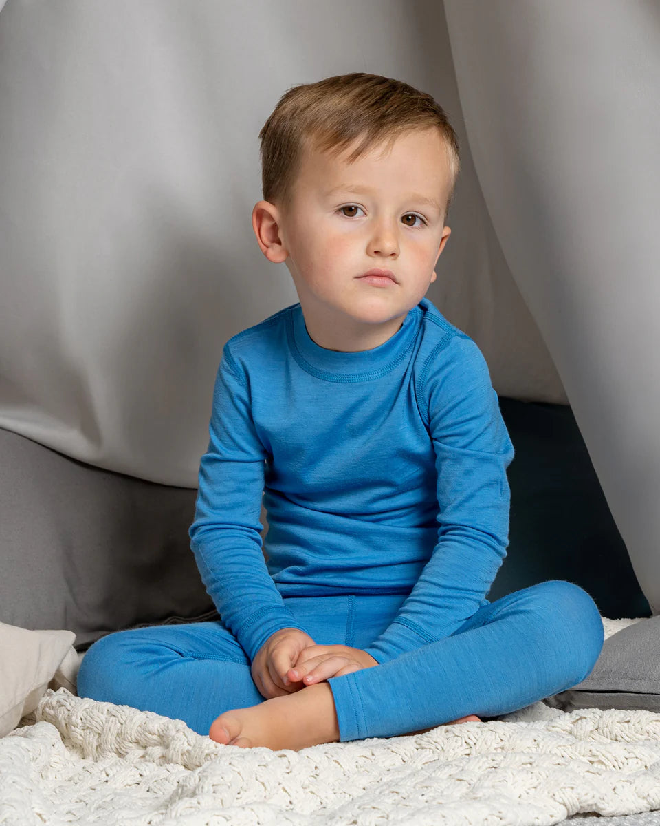 Child wearing blue pajamas sitting on a bed with a neutral background