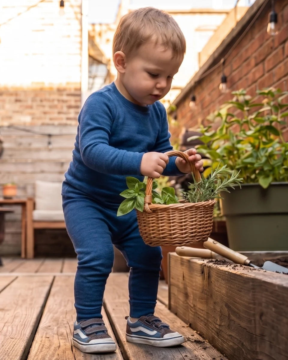 Child in blue outfit gardening outdoors with plants and tools.