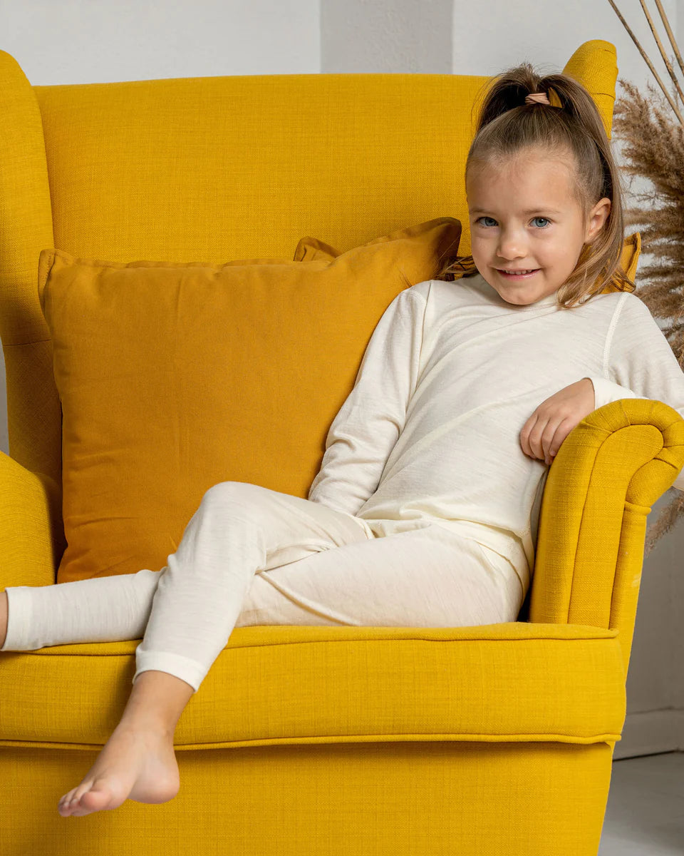 Young girl in a white outfit sitting on a yellow armchair.
