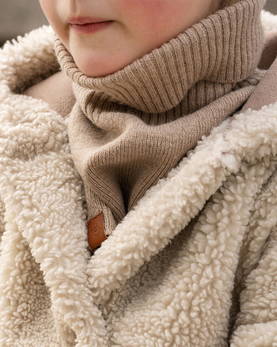 Close-up of a child wearing a beige knitted merino dickie bib