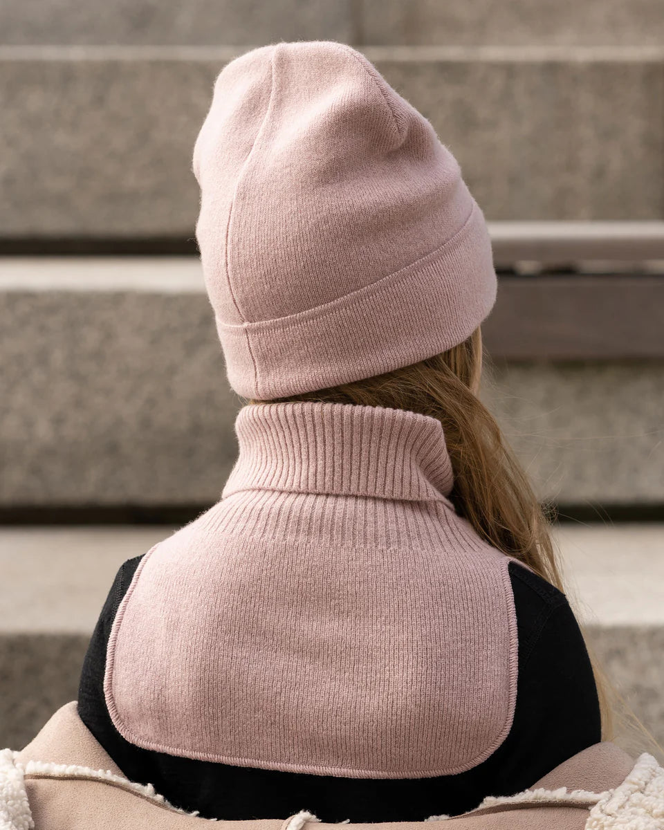 Child wearing a dusty pink knitted merino dickie bib, standing outdoors