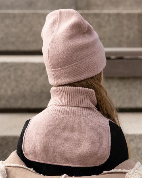 Child wearing a dusty pink knitted merino dickie bib, standing outdoors
