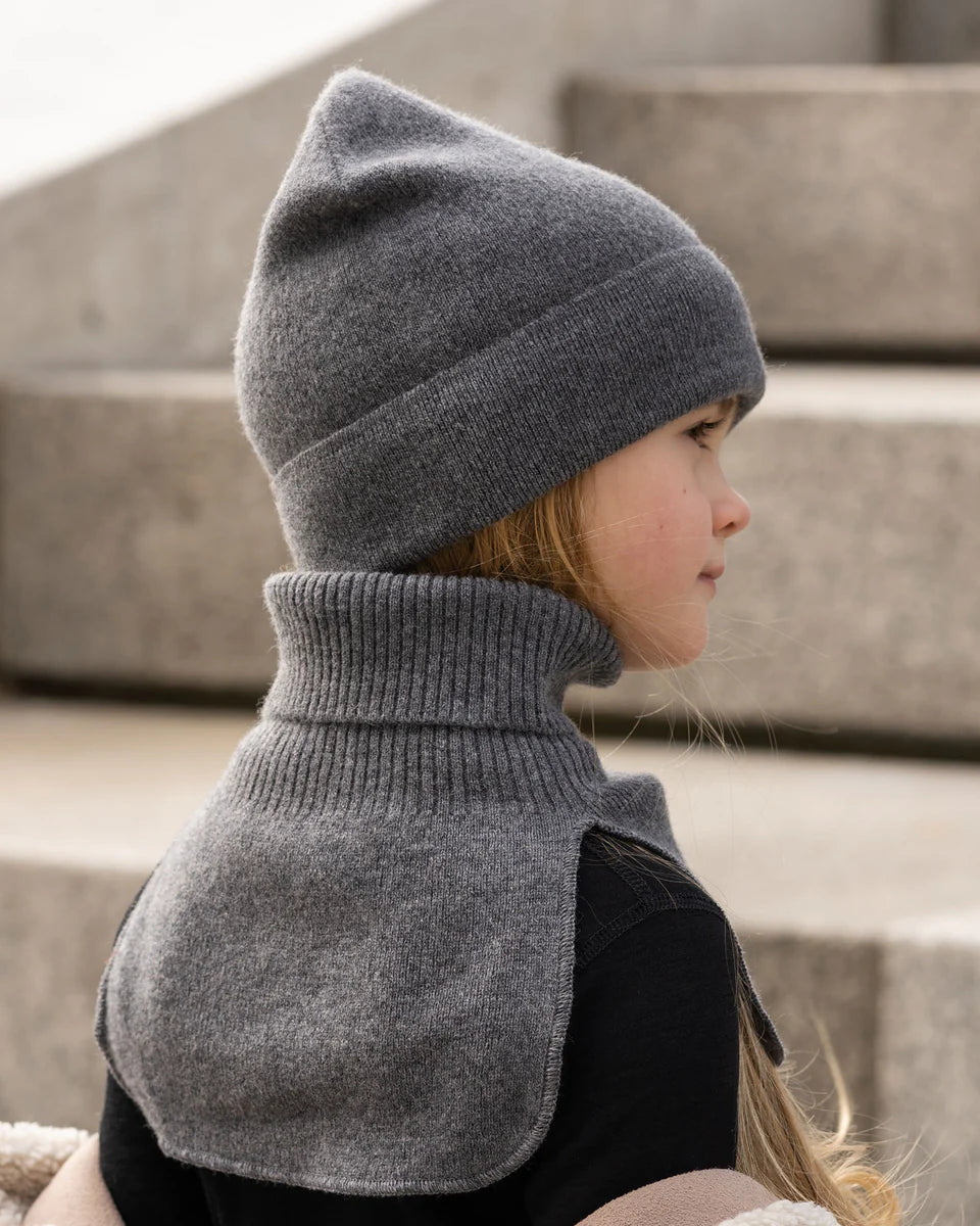Child wearing a dark gray knitted merino dickie bib, sitting outdoors