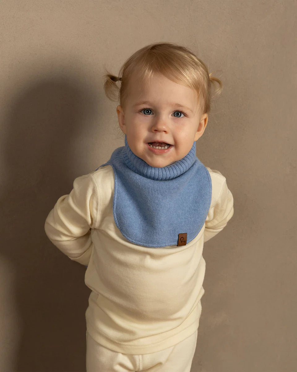 Child wearing a blue bib with a brown brand logo on a beige background