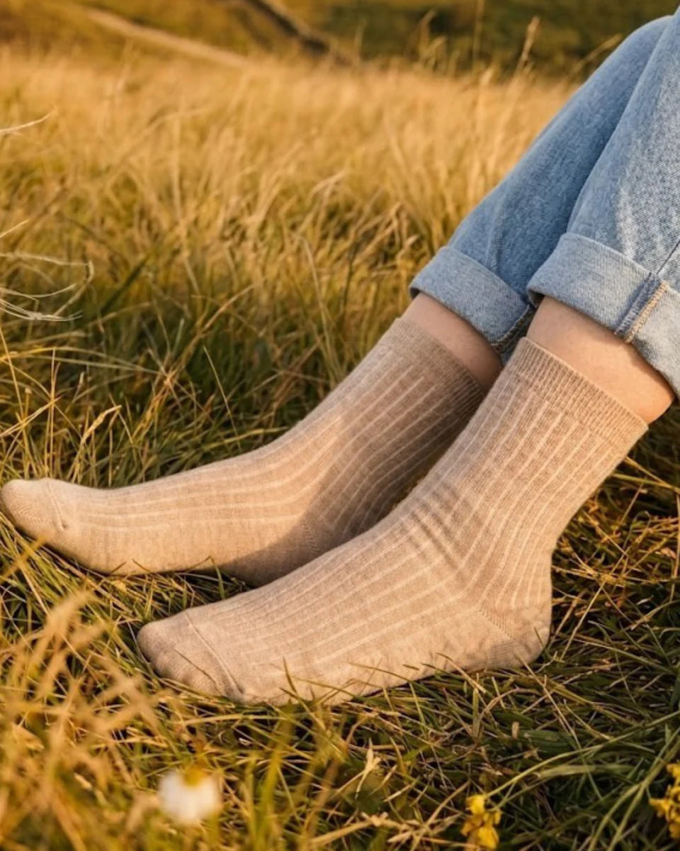 Person wearing beige socks and rolled-up jeans sitting in a grassy field.