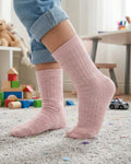 Child wearing pink socks in a playroom with toys and a table in the background