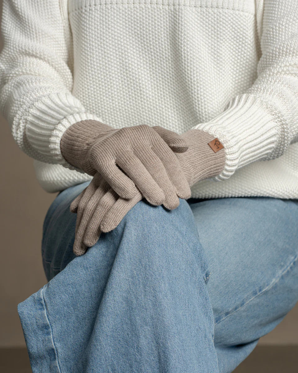 Person wearing beige gloves and a white sweater with a brown background