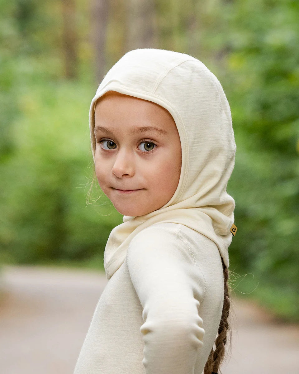 Child wearing a beige hijab with a blurred green forest background