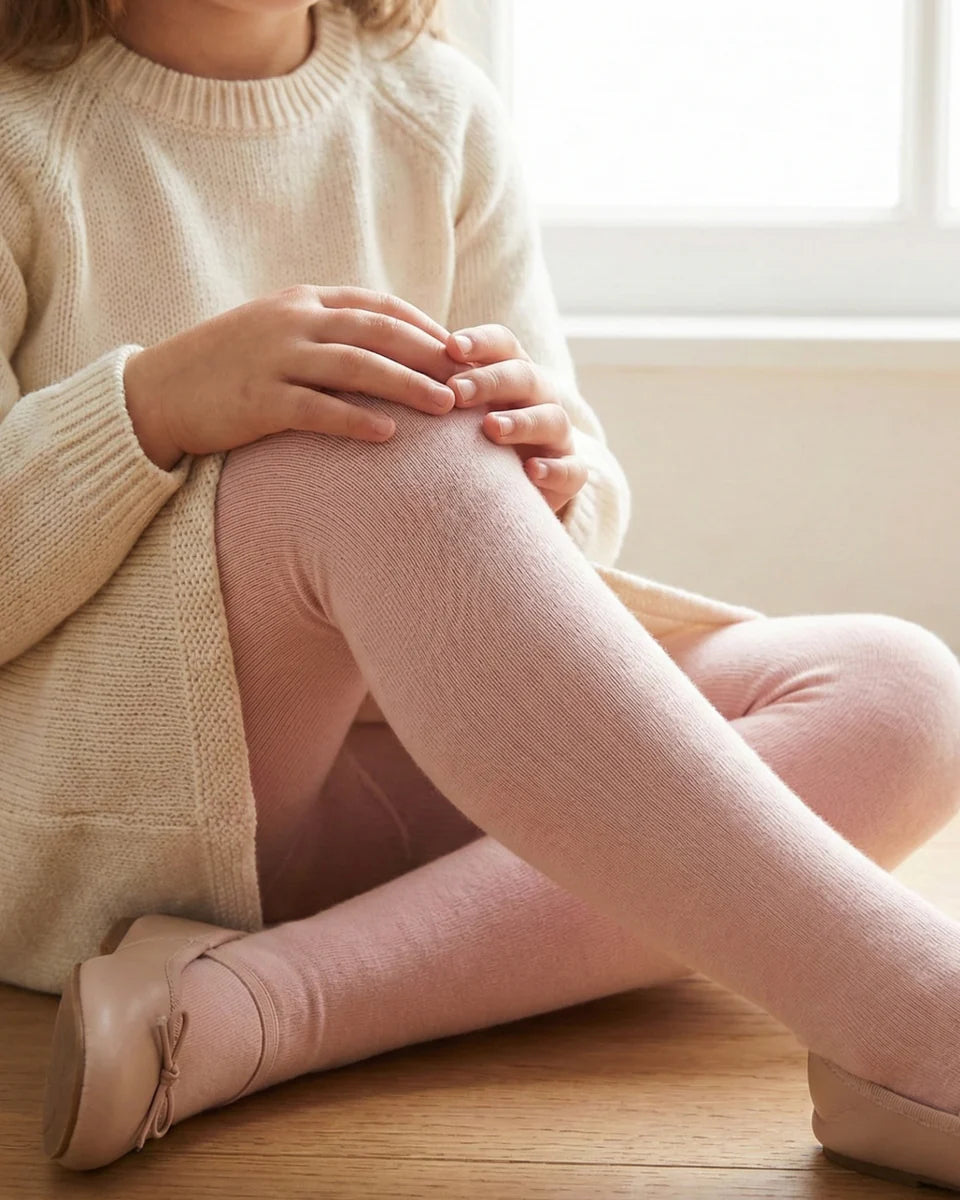 Person wearing a beige sweater and pink tights sitting on a wooden floor.