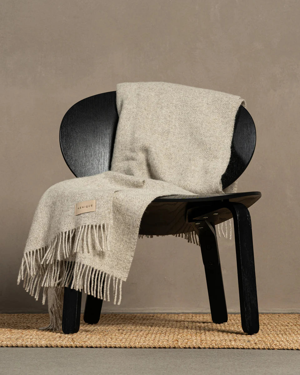 Black chair with a beige blanket draped over it against a plain wall.