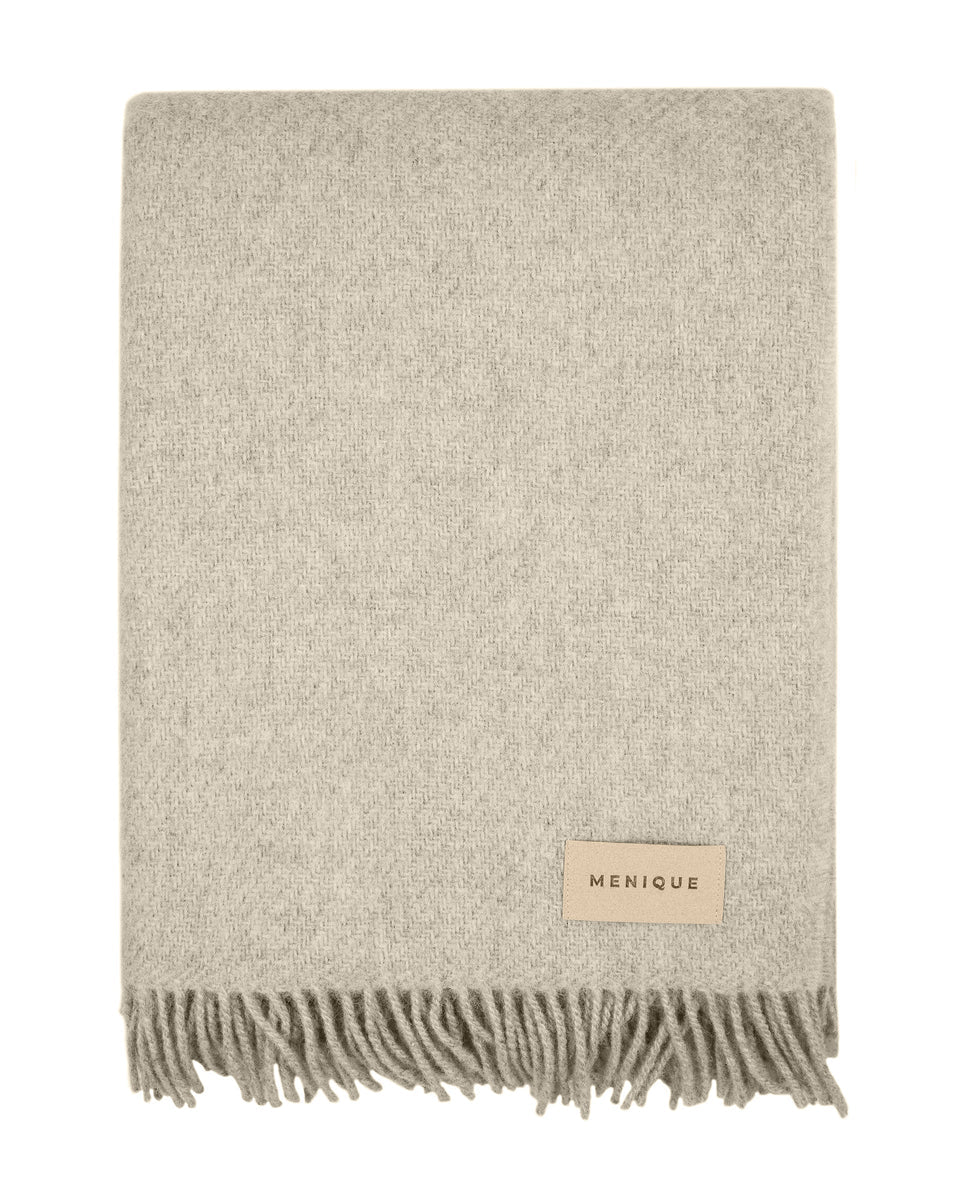 Beige woven blanket with fringes and a brand label on a white background