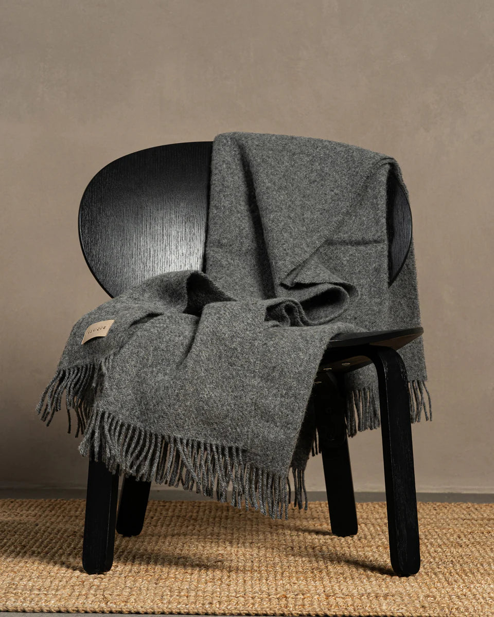 Gray blanket draped over a black chair against a neutral background