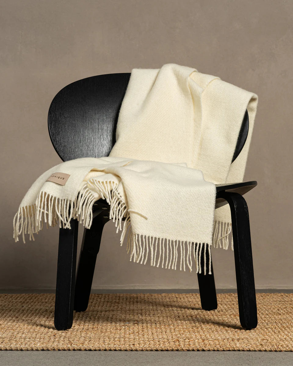 Black chair with a white blanket draped over it against a beige wall.