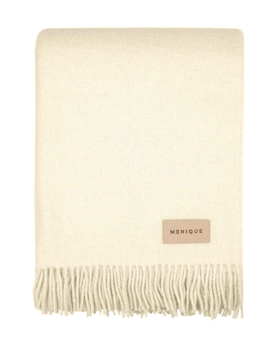 Cream-colored throw blanket with fringes and 'Menique' label on a white background